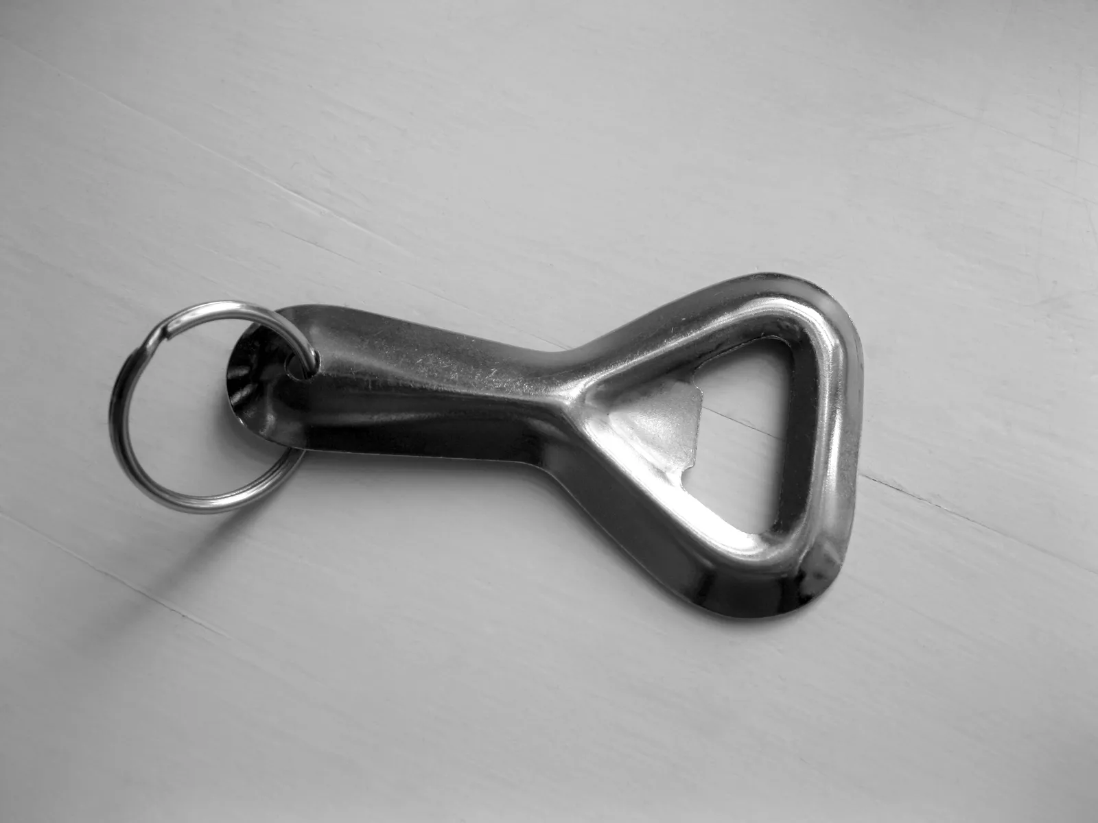 A plain metal bottle opener keychain with a split ring, lying on a light wooden table
