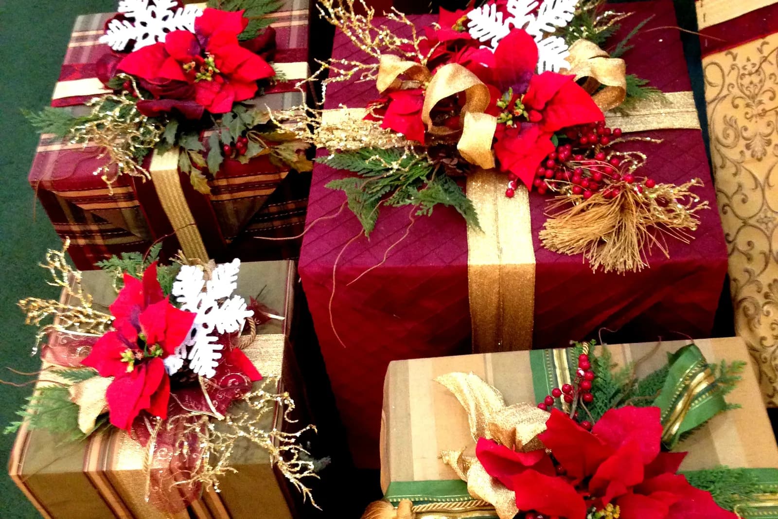 Christmas presents wrapped in red and gold paper, tied with ribbon and topped with red poinsettias and white snowflakes