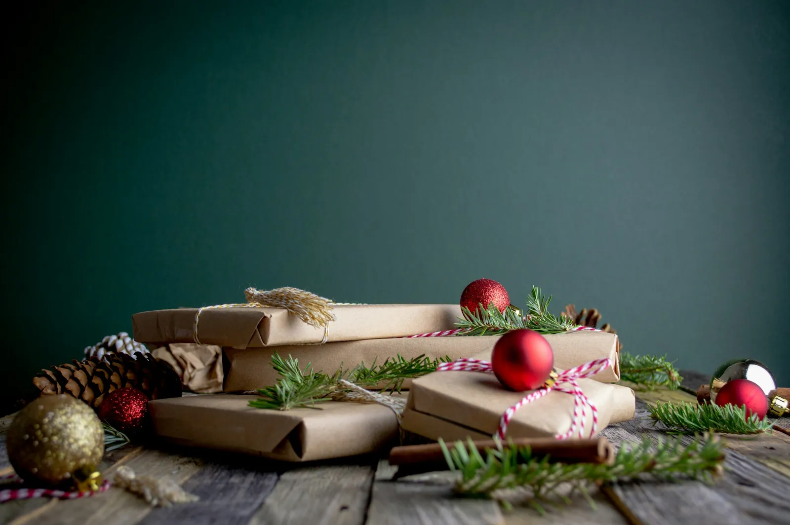 Kraft-paper wrapped gifts with red baubles and pine sprigs on a rustic wooden table