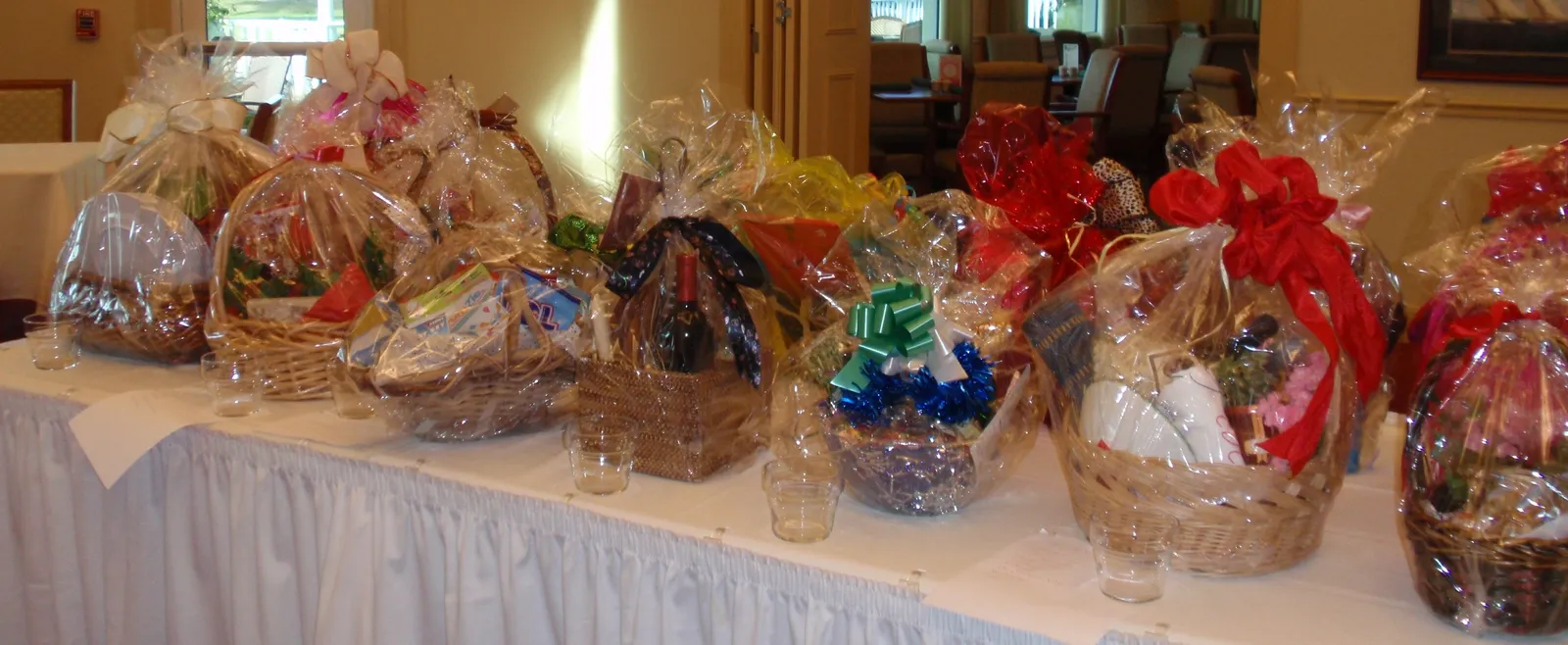 A long table of gift baskets wrapped in clear cellophane and tied with red, green and white ribbons, ready for a raffle