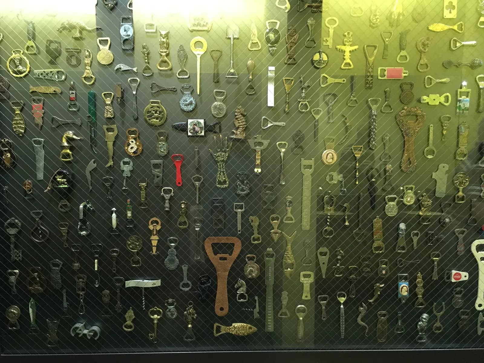 A large wall display of dozens of vintage and novelty bottle openers behind glass