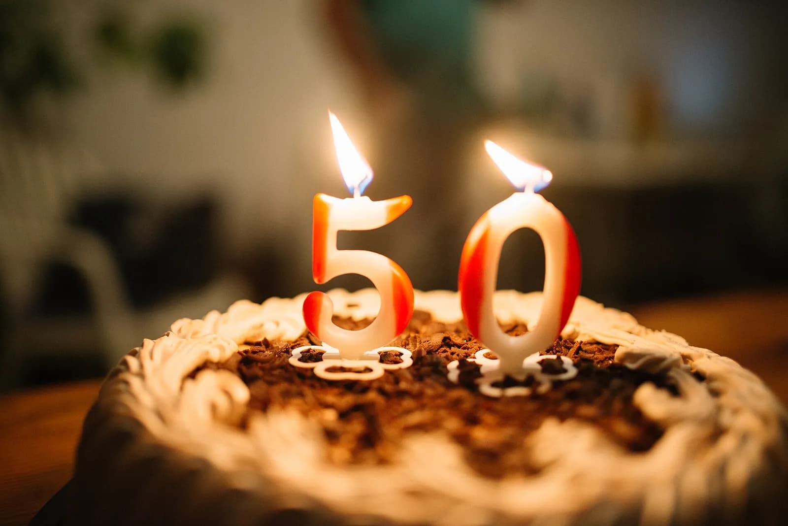 A birthday cake topped with chocolate shavings and two lit number candles forming the number 50