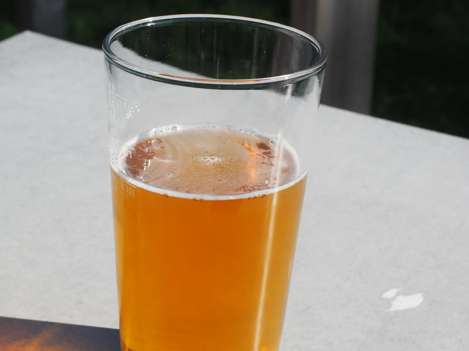 A straight pint glass of golden alcohol-free beer with a thin head of foam on a sunlit outdoor table