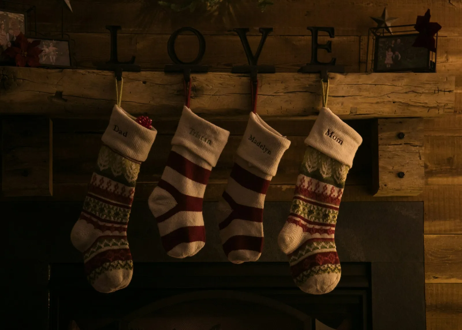 Four knitted Christmas stockings hanging from a wooden fireplace mantel