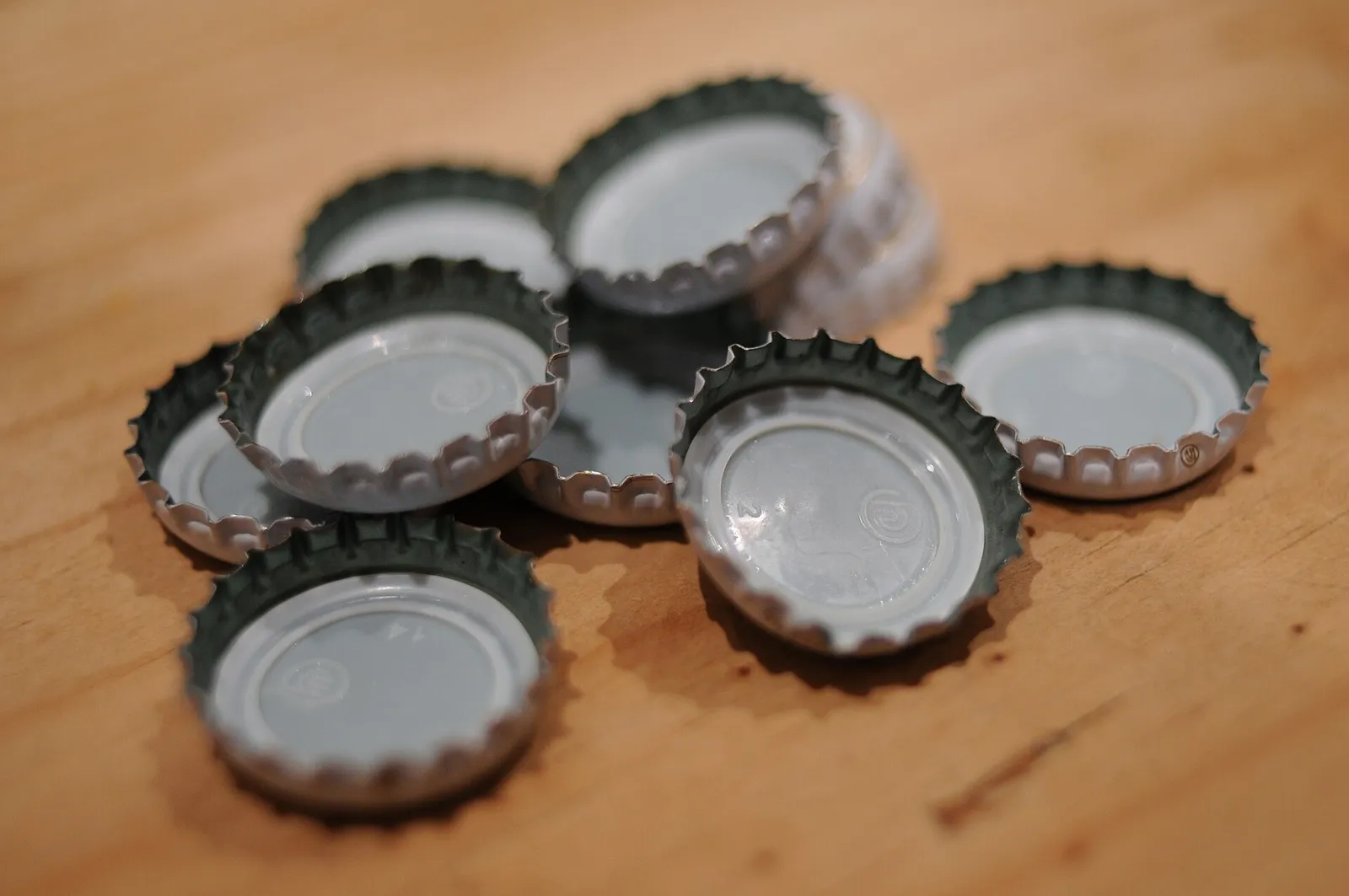 A handful of metal crown bottle caps lying upside down on a wooden table