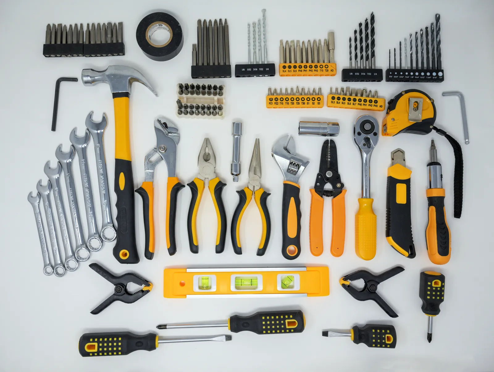 A hand tool set laid out on a white surface: hammer, pliers, wrenches, screwdrivers, a tape measure, a level and boxes of bits