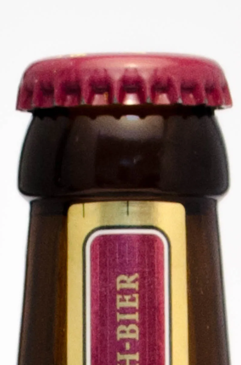 Close-up of a red metal crown cap crimped over the lip of a brown glass beer bottle